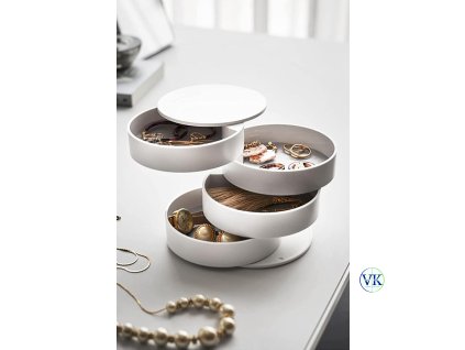 Fehér, forgatható ékszertartó doboz, több rekesszel, asztalon elhelyezve, tele ékszerekkel.